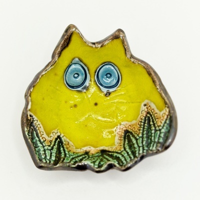 Peça decorativa cerâmica amarela com olhos azuis e detalhes verdes tipo plantas