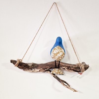 Pássaro decorativo em tecido azul e amarelo pendurado num ramo de madeira