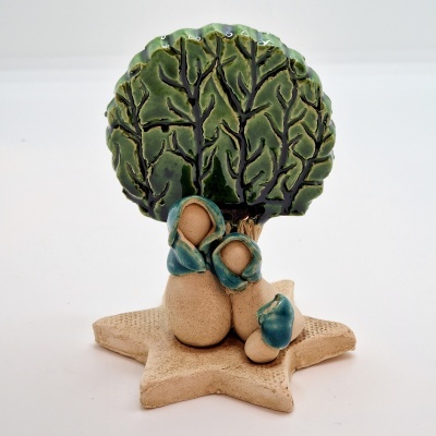 Escultura cerâmica com 3 figuras abstratas sentadas e árvore verde ao fundo