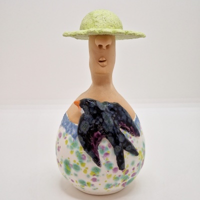 Estatueta em cerâmica com chapéu verde, rosto minimalista e pássaro preto em relevo.