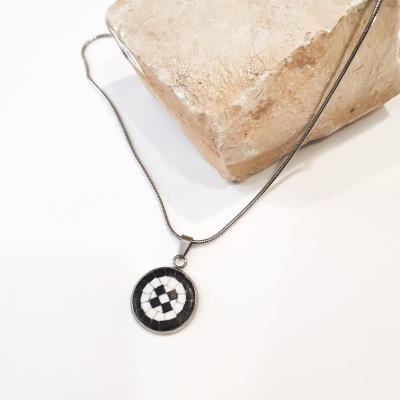 Colar com pendente redondo xadrez preto e branco sobre superfície branca e pedra bege