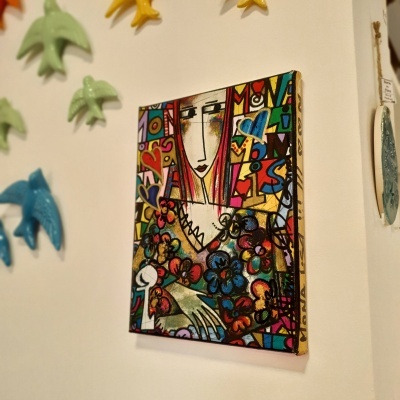 Quadro colorido com pintura estilizada de mulher e pássaros de cerâmica na parede