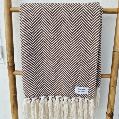 Manta castanha e branca com padrão ziguezague e franja numa estrutura de madeira