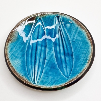 Prato de cerâmica azul com borda castanha e desenhos em relevo no centro