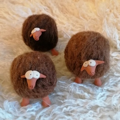 Três ovelhas decorativas de lã castanha com patas e focinhos cor de terracota sobre tecido branco felpudo