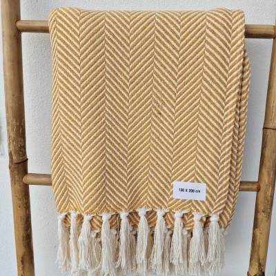 Manta têxtil mostarda e branca com padrão espinha de peixe e franjas pendurada numa estrutura de madeira