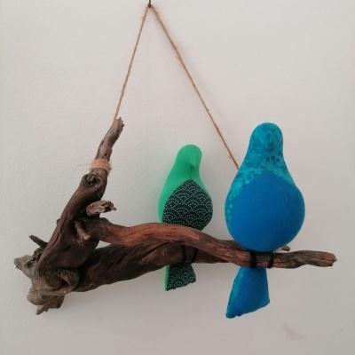 Decoração de dois pássaros de tecido verde e azul em madeira rústica pendurada numa parede branca