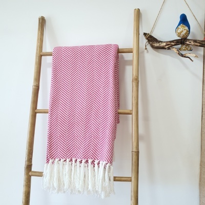 Manta chevron rosa e branca com franjas pendurada em cabide de madeira com pássaro decorativo ao lado