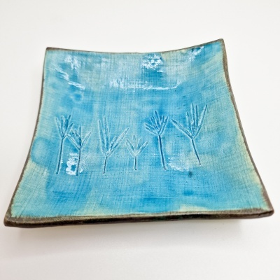 Prato cerâmico quadrado azul com padrão de folhas gravadas.