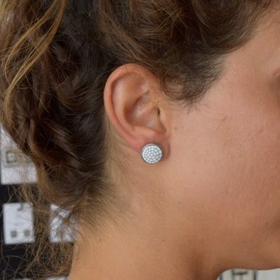 Brinco redondo prateado com padrão branco hexagonal na orelha de mulher