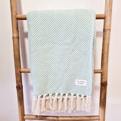 Manta azul claro com padrão espinha de peixe e franjas pendurada em escada de madeira