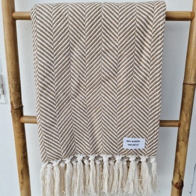 Manta de algodão bege clara e castanha com franjas pendurada numa estrutura de madeira