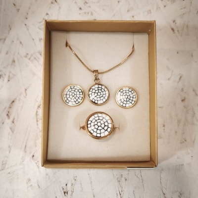 Conjunto de joias dourado com padrão branco rachado, numa caixa bege.