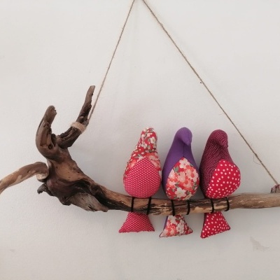 Três pássaros decorativos em tecido pendurados em galho de madeira