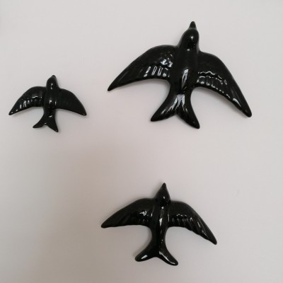 Três pássaros pretos brilhantes de diferentes tamanhos numa superfície branca.