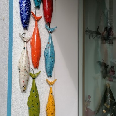 Peixes decorativos coloridos em cerâmica pendurados numa parede branca ao lado de uma porta de vidro