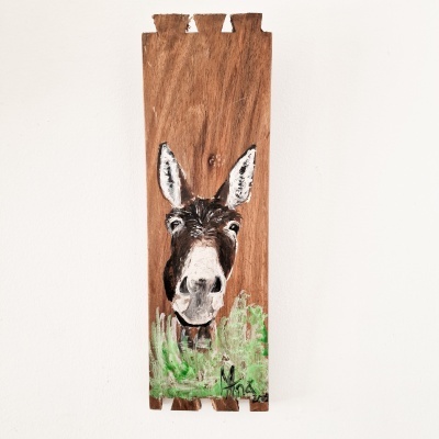 Tábua de madeira pintada com o rosto de um burro e plantas verdes