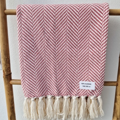 Manta vermelha e branca com franjas pendurada numa escada de madeira.