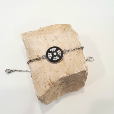 Pulseira prateada com pendente preto e branco sobre pedra bege