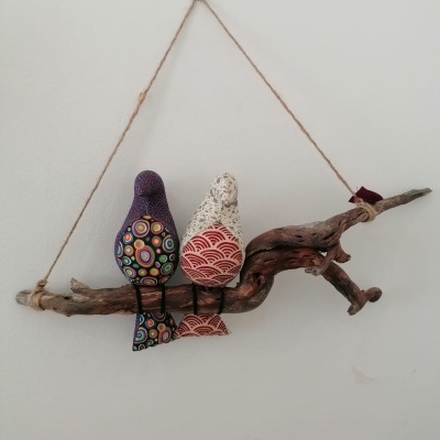 Decoração de parede com dois pássaros de tecido colorido pendurados num ramo de madeira.