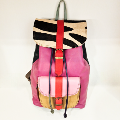 Mochila rosa com bolso bege e rosa claro, fechos vermelhos, tampa bege com padrão preto, alças verdes