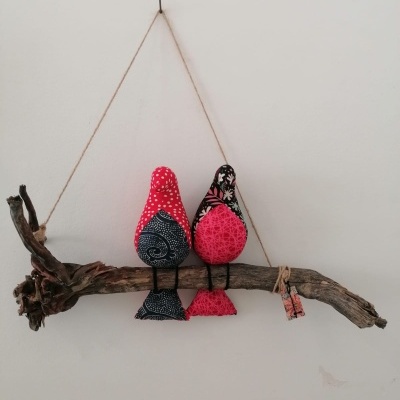 Decoração artesanal de dois pássaros de tecido sentados num ramo de madeira rústica pendurados na parede