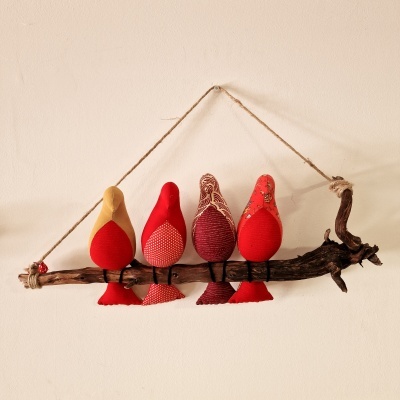 Quatro pássaros de tecido vermelho pendurados numa vara de madeira