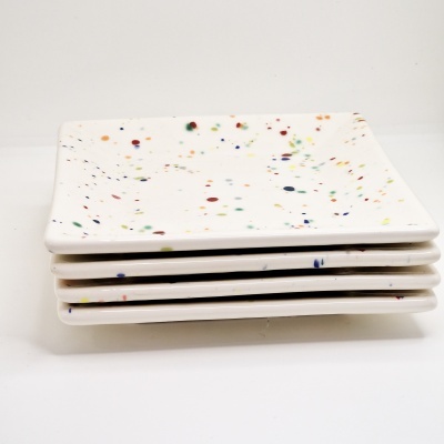 Quatro pratos quadrados brancos com pontos coloridos empilhados sobre fundo branco.