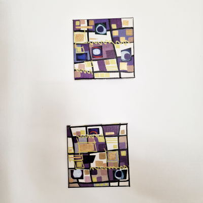 Dois quadros quadrados com padrões geométricos coloridos pendurados numa parede branca