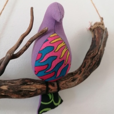 Pássaro decorativo de tecido colorido pendurado num ramo de madeira.