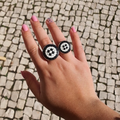 Mão com anéis de padrão de quadrados pretos e brancos sobre calçada portuguesa