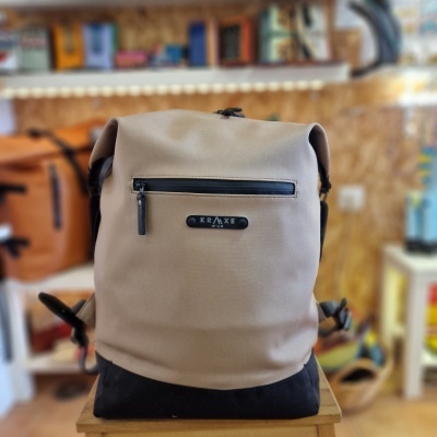Mochila bege e preta com bolso frontal e etiqueta KRAKE