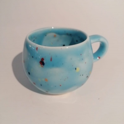Chávena de cerâmica azul clara com manchas coloridas e cabo arredondado