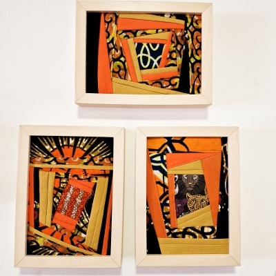 Três quadros com moldura branca e tecidos coloridos laranja e preto com padrões geométricos