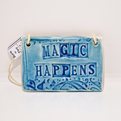 Placa cerâmica azul com texto 'MAGIC HAPPENS' e padrão floral