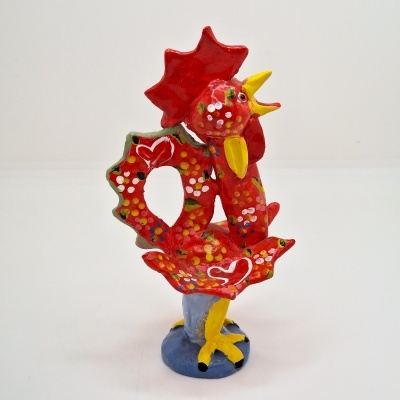 Escultura cerâmica colorida de galo com padrões de bolinhas e corações em base azul.