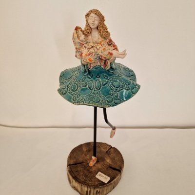 Escultura de mulher com vestido estampado e saia azul sobre base de madeira