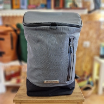 Mochila cinzenta e preta com ziper vertical em mesa de madeira