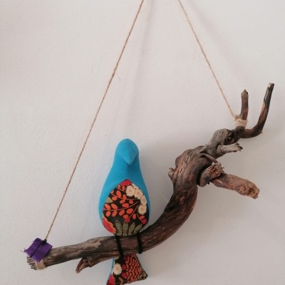 Passaro de tecido azul pendurado em ramo de madeira com corda