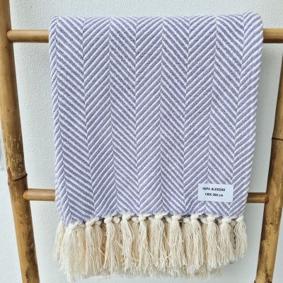 Manta de algodão lilás e branco com padrão em espinha de peixe e franjas, pendurada numa estrutura de bambu