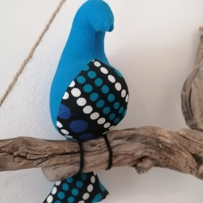Pássaro decorativo de tecido azul e preto com bolinhas sentado num galho de madeira