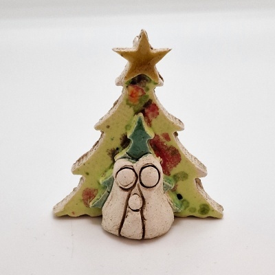 Decoração de Natal em cerâmica com árvore verde, manchas vermelhas, estrela dourada e figura branca à frente com olhos e nariz circulares