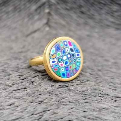 Anel dourado com topo redondo e padrão geométrico colorido