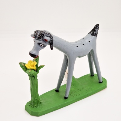 Figurinha de cabra cinzenta cheirando flor amarela numa base verde