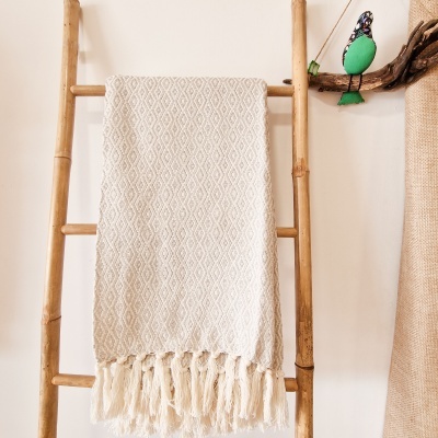 Cobertor creme texturizado com franjas pendurado numa escada de madeira clara