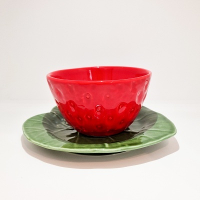 Taça vermelha de cerâmica com textura de morango sobre prato verde com textura de folhas