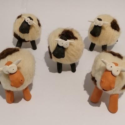 Cinco miniaturas de ovelhas em pelúcia com cores branca, castanha, preta e laranja sobre fundo branco