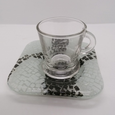 Copo de vidro transparente sobre pires quadrado de vidro com padrão de mosaico cinzento e preto