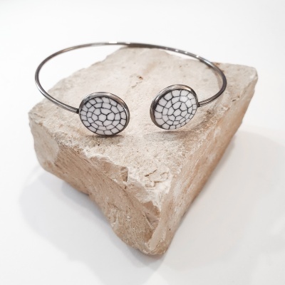 Bracelete metálico com pedras ovais brancas de padrão mosaico preto sobre bloco rústico