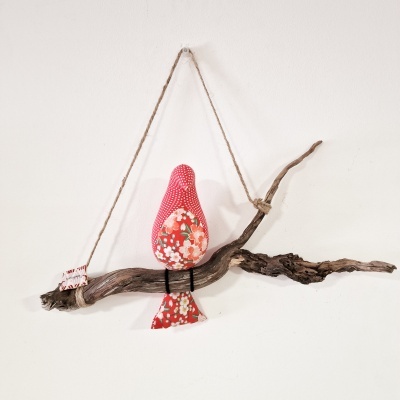 Pássaro decorativo em tecido vermelho com padrão de bolinhas e flores pendurado em galho seco